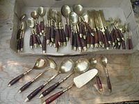Full view of vintage gold plated flatware set with wooden handles arranged together showing variety of items.