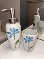 Close-up of ceramic liquid soap dispenser and matching tumbler with blue flower design on bathroom counter