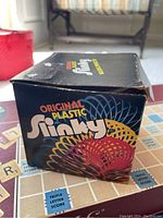 Original Plastic Slinky box showing colorful coils on top of a Scrabble board.