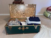 Photo of open green vintage cedar chest showing interior filled with folded womens clothing including sweaters and shirts