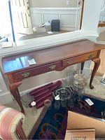 Front and top view showing polished wood surface and two drawers with brass handles against a white wall.