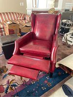 Red leather recliner chair with footrest extended, placed on a patterned rug in a living room with other furniture and boxes in background.