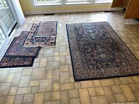 Five navy blue patterned rugs with red and tan floral accents arranged on tiled floor, showing size variation and patterns.