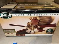 Original packaging box of Hunter Coastal Breeze Plus ceiling fan showing brand, model, size, features, and image of assembled fan.