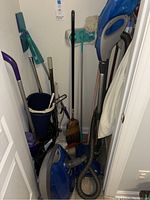 Laundry room with upright Kenmore canister vacuum, multiple mops, broom, mop bucket, toilet brushes, and fly swatter visible.