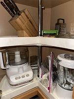 White KitchenAid food processor and blender on kitchen corner shelf with knife block, grater, orange juicer, and utensils around