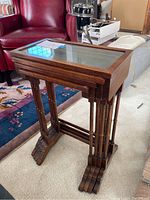 Side view of the set of four wood nesting tables with glass tops showing the largest table on top of the smaller nested tables.