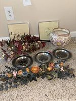 Photo of the full lot on carpet: two framed floral wall art pieces, faux eucalyptus spray, a floral spray, a ceramic floral vase, and three pewter plates