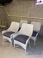 Four large white wicker chairs with blue and white striped cushions arranged in a basement area with concrete floor and walls.