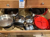 Drawer containing various pots and pans, visible red Dansk soup pot, various Farberware pots and pans, and lids.