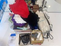 Wide view of assortment including scarves in various colors, white gloves in packaging, small handbag, blue rosary, and gold-tone bracelet on white surface.