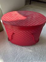 Red oval-shaped quilted sewing box on carpeted floor