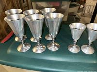 Six silver metal goblets with textured stems and smooth conical bowls placed on a table surface.