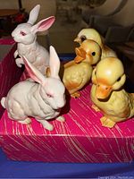 Photo of five ceramic spring decor figurines on a pink box; two rabbits and three ducklings.