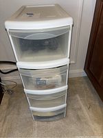 Four white plastic stacking drawers against a wall with visible cords inside drawers.