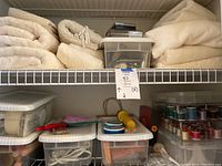 Shelf with folded cream-colored towels stacked along with clear plastic containers holding sewing supplies such as spools of thread and notions.