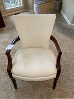 Front view of cream-colored upholstered armchair with button tufting and wooden frame