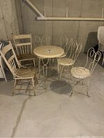 Full lot of vintage metal bistro table with four matching chairs plus two additional wooden chairs in basement setting.