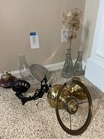 Full lot overview showing vintage oil lamp sconce with chimney and reflector, brass electric sconce, three glass vases, and dried flower stems on floor against wall.