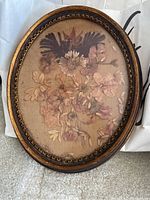 Oval ornate wooden frame with dried flowers pressed underneath glass, showing entire piece against a neutral background.