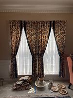 Three floral pattern pinch pleat window treatment panels framing three windows with sheers behind; panels are bounded with dark trim.