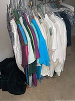 View of assorted tops on hangers showing colors from white, purple, teal, green, blue, to patterned designs.