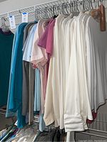 Photo showing a row of women's casual tops on hangers with mostly white and light-colored long-sleeve shirts and some short-sleeve tops in the background.
