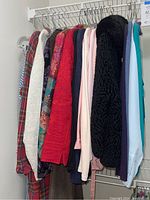 Photo showing a rack of women's long sleeve tops and jackets in various colors and patterns including plaid, solid colors, and knitwear.