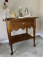 Front view of mid-toned wood side table with various items on top including trophies, figurines, basket, and bud vase.