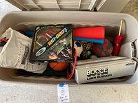 Top view of large storage bin filled with various yard games and balls including bocce lawn bowling set, dodgeball game, and assorted sports balls.