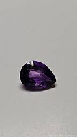 Photo of single pear cut deep purple Brazilian amethyst gemstone showing facet reflections and clarity features