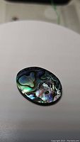 Oval shaped natural abalone doublet cabochon photographed on a plain light surface showing colorful iridescent swirling patterns.