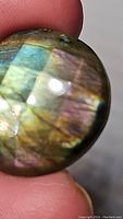 Close-up image showing the round labradorite gemstone with checkerboard cut and colorful iridescence including blue and gold hues.