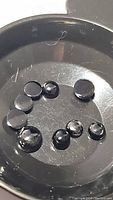 Seven round cabochon jet black onyx stones of varying sizes in a black container.