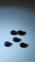 Photo of five natural oval cut blue sapphires on white background, showing shape, size, and color.