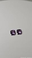 Two cushion checkerboard cut Brazilian amethyst gemstones shown on a white background.