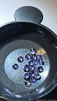 Top view of multiple small round purple iolite cabochon gemstones in a black dish, showing size and color.
