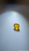 Oval cut yellow sapphire gemstone photographed under spotlight showing deep golden yellow color and internal reflections.