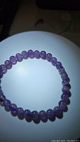 Full view of amethyst bead bracelet displayed on white surface, showing round polished beads and elastic band.