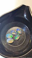 Five oval cabochon cut Ethiopian crystal opal stones exhibiting play-of-color on a black dish.