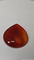Close-up of large, polished, deep fire orange carnelian gemstone on white background, showing rich translucent color and smooth surface.