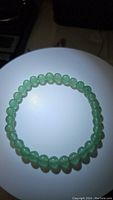 Top-down photo of natural green Aventurine bead bracelet on a white surface highlighting the round beads and their translucent green color.