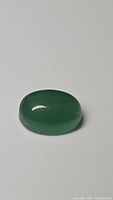 Oval cabochon cut green aventurine gemstone on a neutral background showing smooth polished surface and natural translucence.