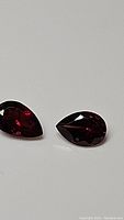 Close-up front view of the pair of deep red pear-shaped garnet gemstones on a plain background showing their faceted surfaces and color.