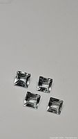 Four natural square cut aquamarine gemstones displayed on a neutral background showing clarity and cut facets.