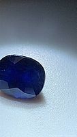 Close-up photo of an oval cut deep royal blue African sapphire gemstone showing its color and faceting details under lighting.