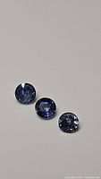 Three natural round cut blue sapphires placed in line on a neutral background showing different blue tones and surface reflections.