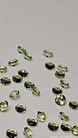 Close-up photo showing scattered small round brilliant cut apple green peridot gemstones, highlighting their clarity and faceted cuts.
