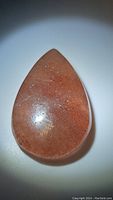 Front view of the natural pear-shaped strawberry quartz cabochon gemstone showing the pinkish internal inclusions and polished surface with minor imperfections.