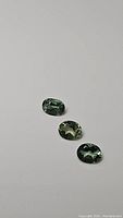 Three natural mint green oval cut apatite gemstones laid flat on a plain background showing color and facets.